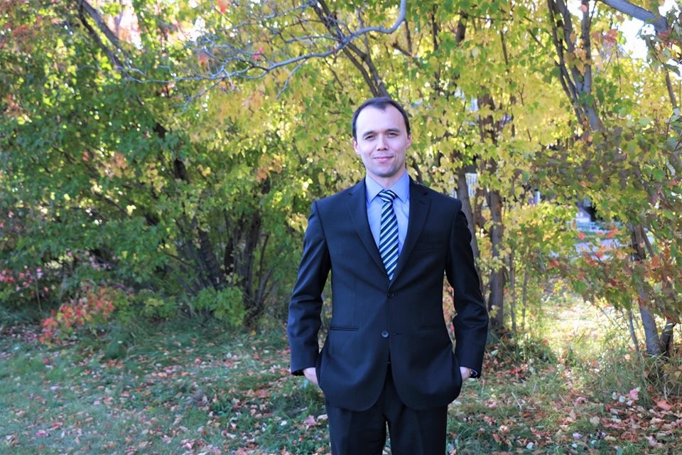 University of Alberta law student Justin Hjlesvold poses for a picture amongst trees wearing a black suit.