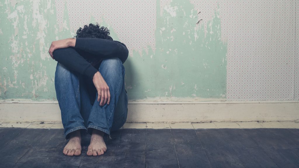 Person sitting against a wall with head buried in arms