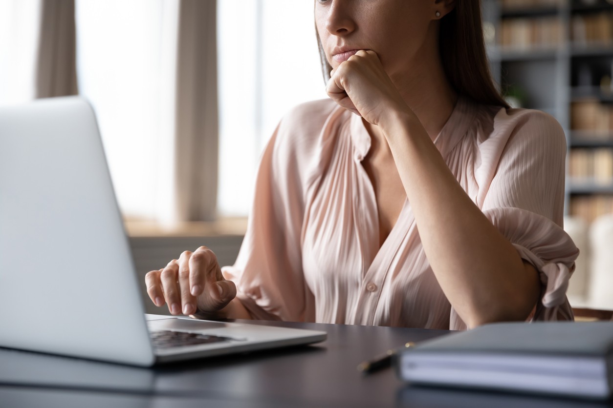 Close up cropped image thoughtful young woman propping head with hand, looking at computer screen. Serious concentrated successful businesswoman working remotely on laptop at office or home.