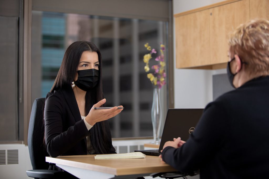 Two women wearing face masks meet in an office.