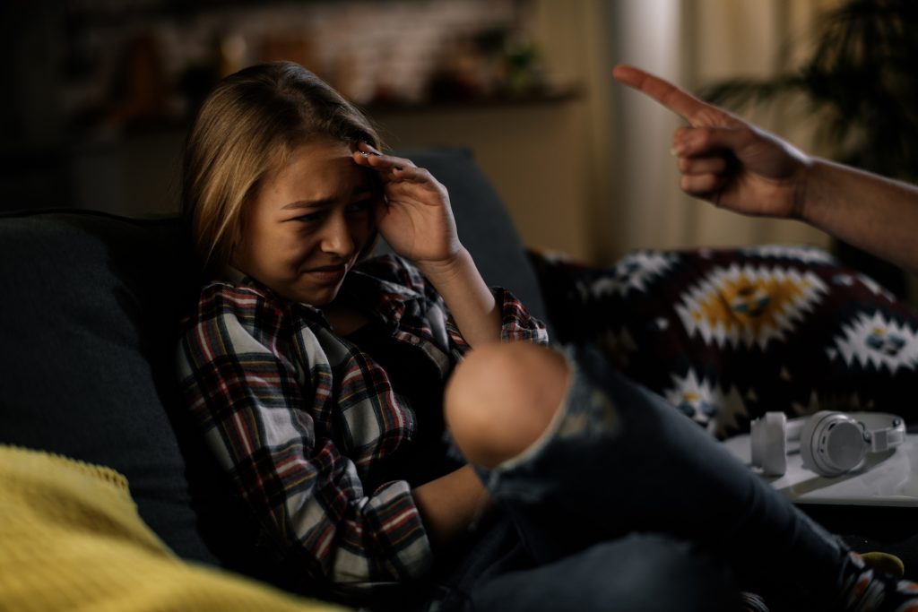 Girl cowering from unseen adult whose had and forearm are in frame, pointing at her. Physical abuse is implied.