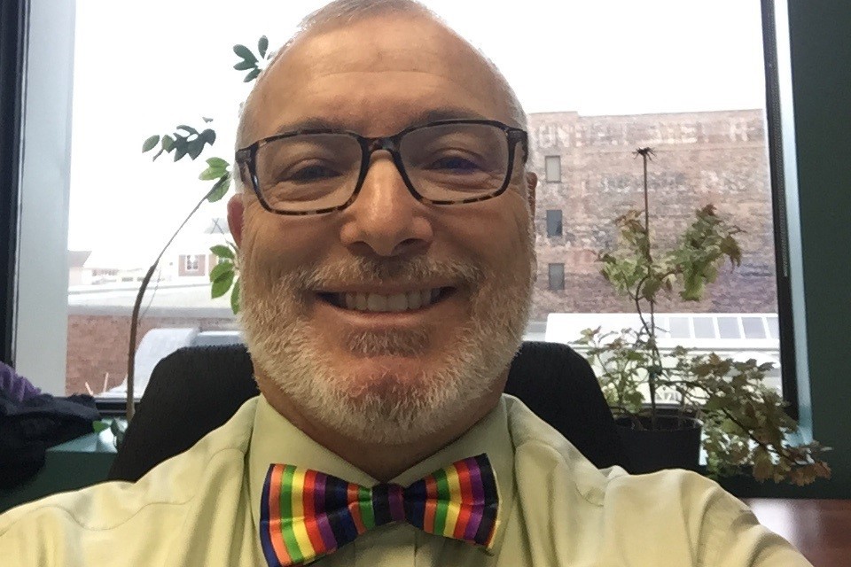 LAA lawyer Chuck Easton takes a selfie at his desk, wearing a rainbow-coloured bow tie