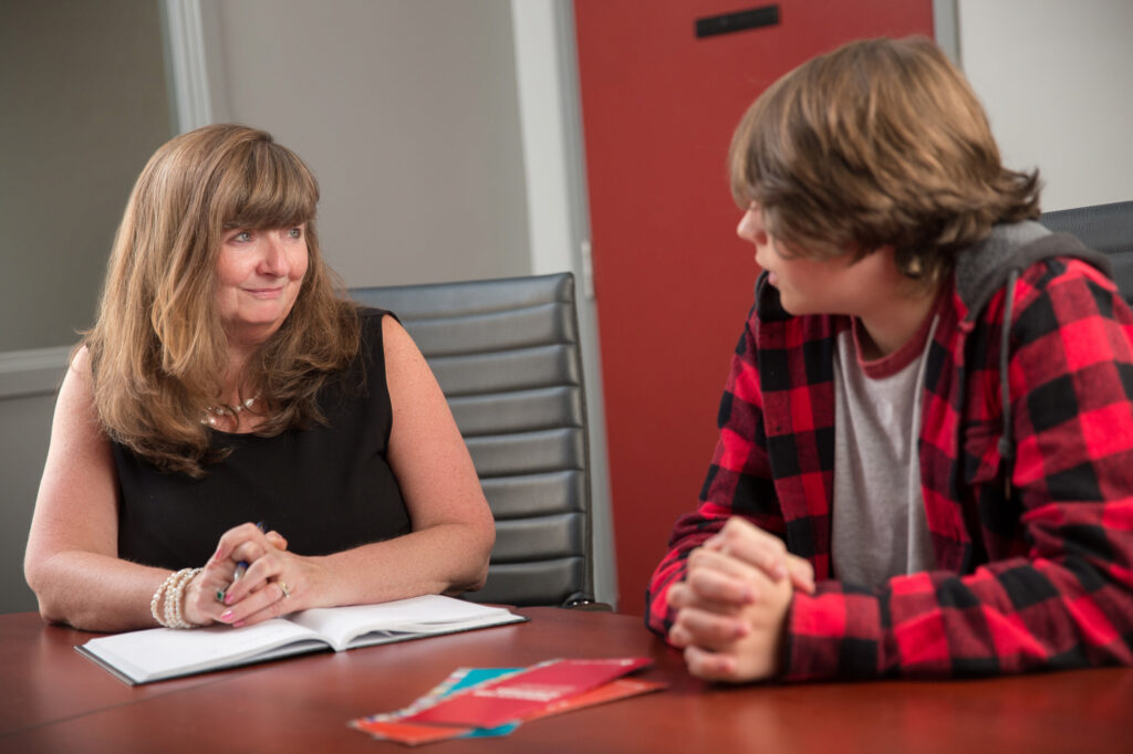 A lawyer and teenage client sit at a table to discuss a legal matter.