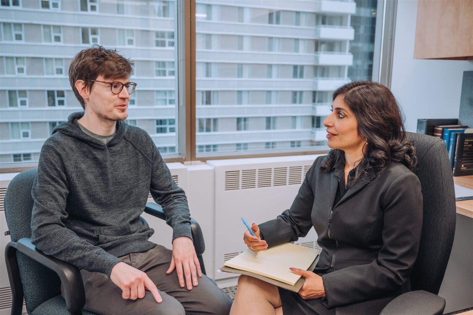 Female lawyer in office chair holding a pad and pen speaking with a young male client