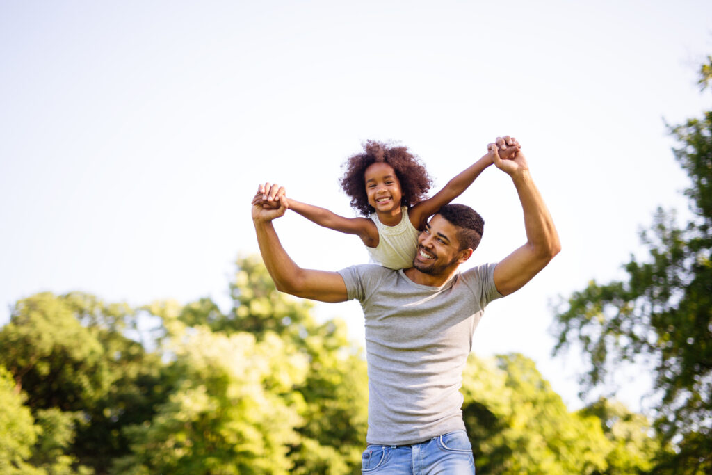 Portrait of father carrying daughter on back outdoors.